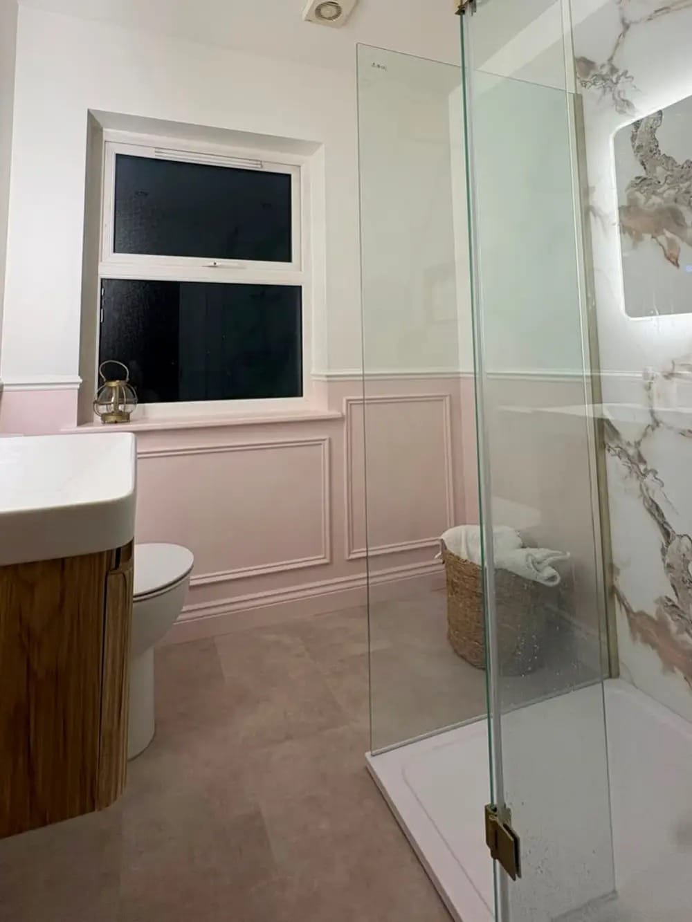 Pink bathroom wall panelling with classical mouldings beside a walk-in marble shower