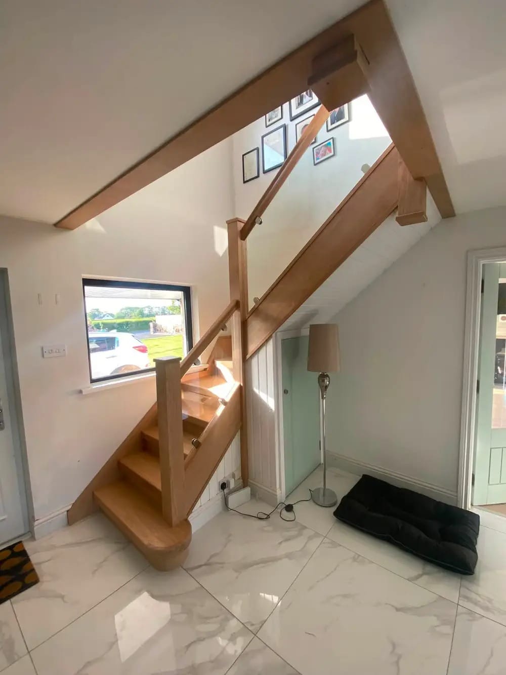 Oak staircase with glass balustrade seen from the entrance hall, sunlight through the window